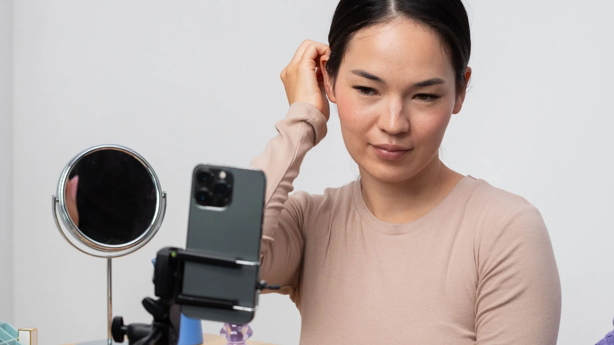 A woman records herself with a smartphone on a tripod while looking in a mirror nearby.