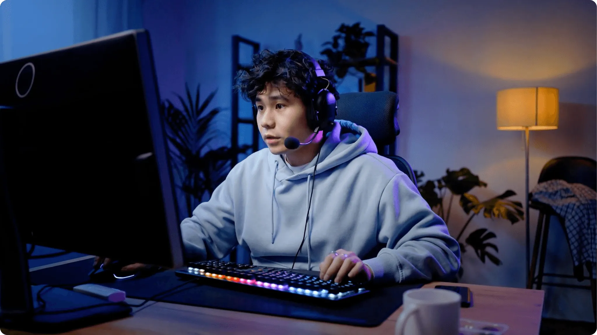 A young person gaming intensely in a dim room while wearing a headset and using an RGB keyboard.