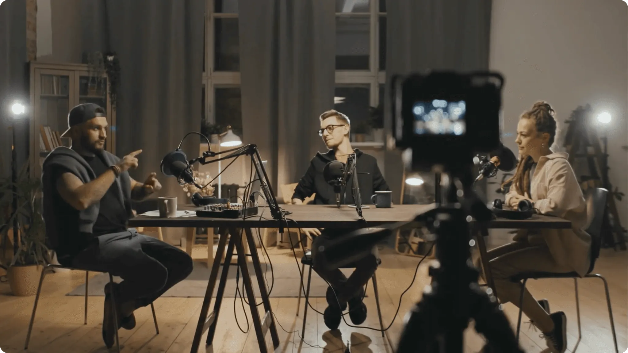 Three people sitting around a table recording a podcast with microphones and a camera.